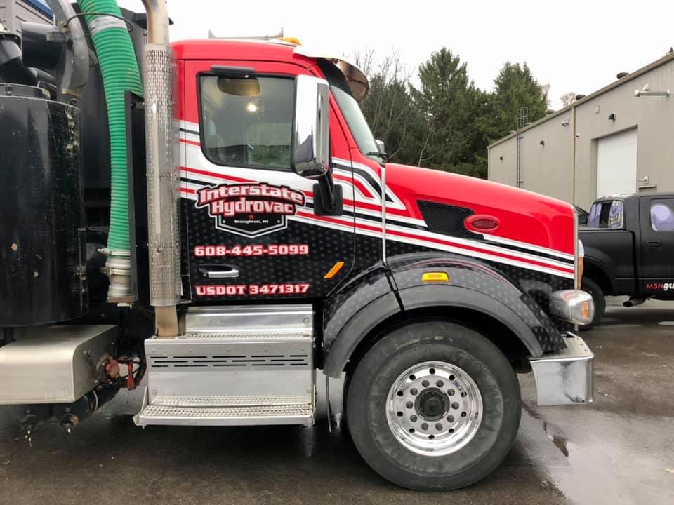 Red, white and black vehicle wrap design on a large truck cab promoting a hydrovac service