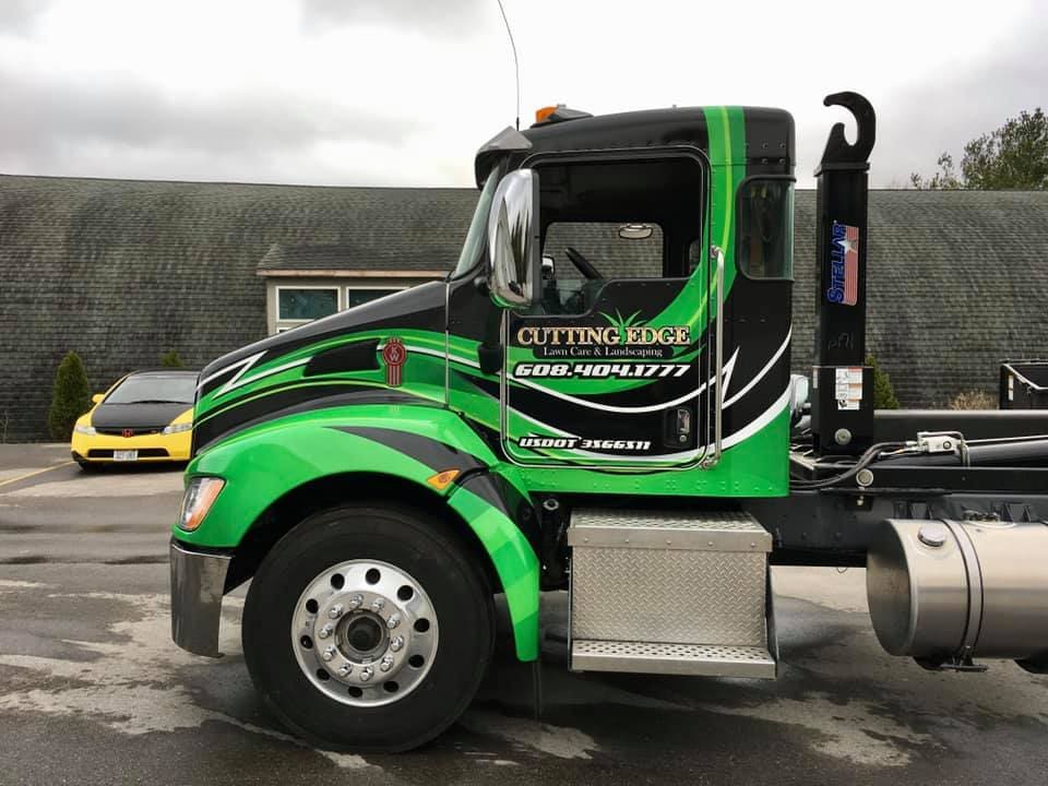 Green and black vehicle wrap design on a large truck cab promoting a landscaping services