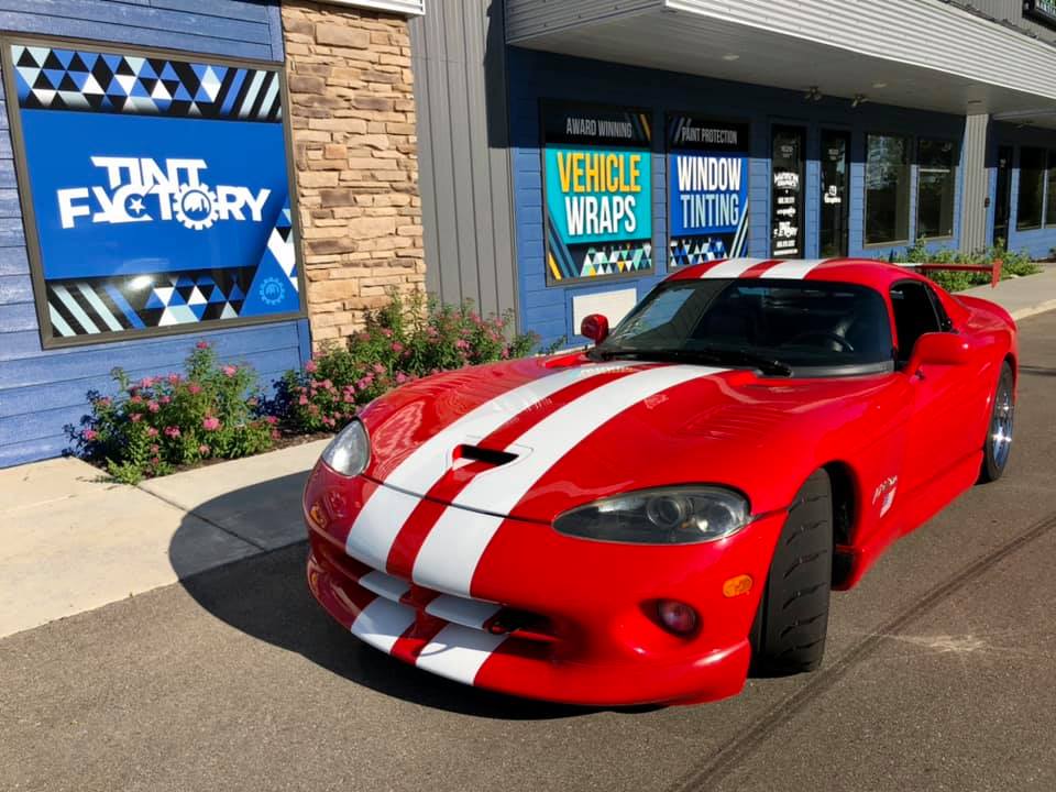 Red racing car with 2 white stripes parked in front of Madison Graphics company tint factory in Madison Wisconsin