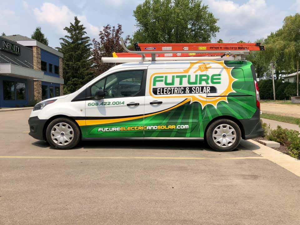 A green van featuring Fleet Wraps and Graphics for “Future electric & solar” is parked in a lot. The company’s contact info, cityscape, sun design, and plug graphics are proudly displayed on the side.