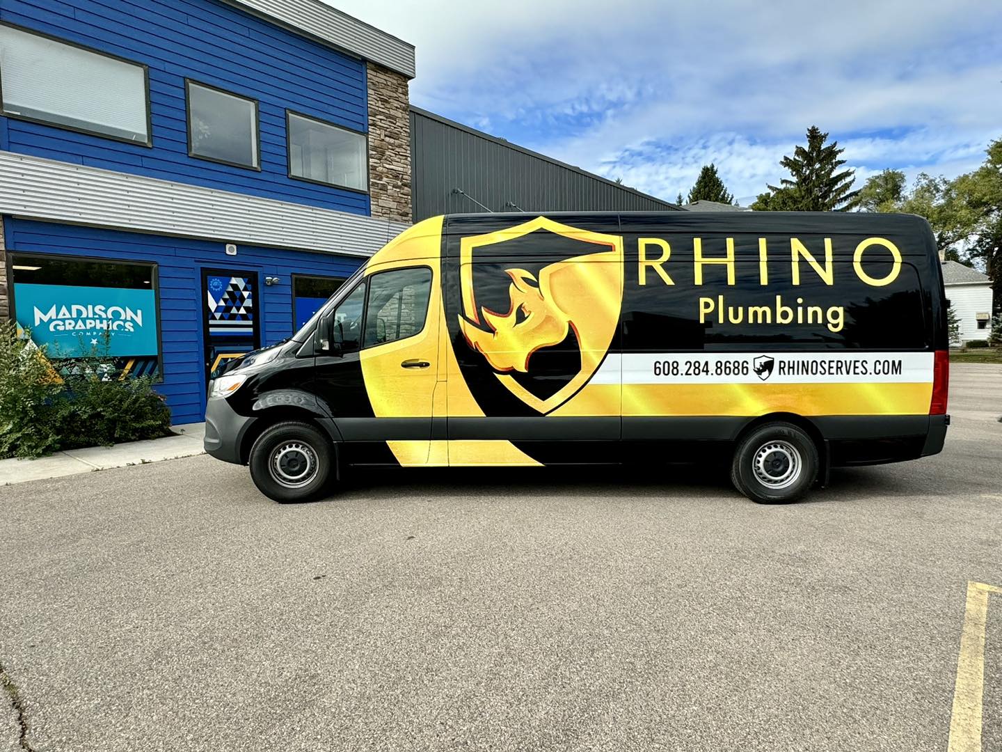 Black and gold Rhino plumbing van, featuring custom fleet graphics, parked in a lot for Madison Graphics. The van shows the phone number and website