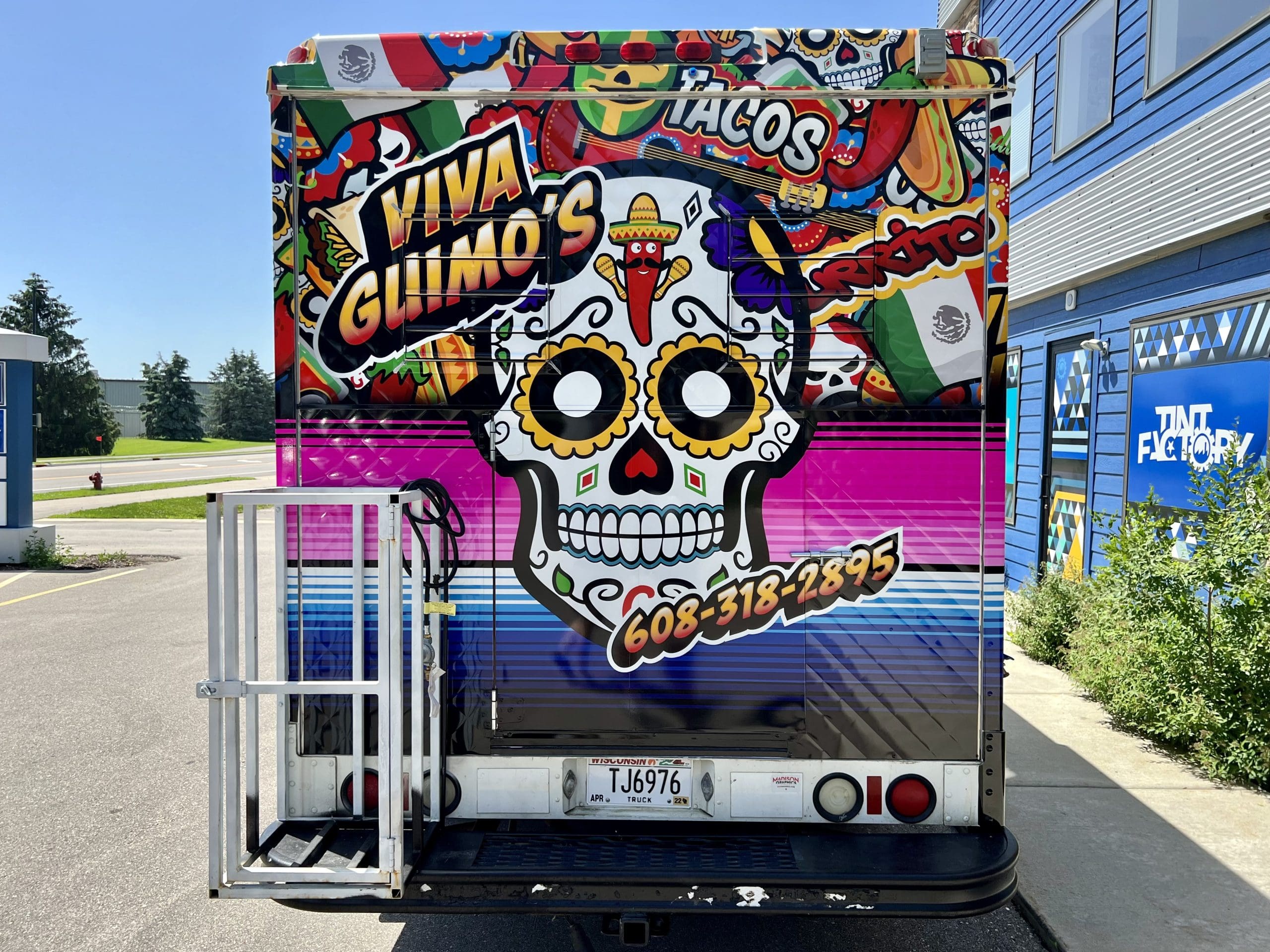 Back of Mexican restaurant food truck with fun vehicle wrap with a Mexican skull cartoon and chili shaking maracas featuring the company phone number