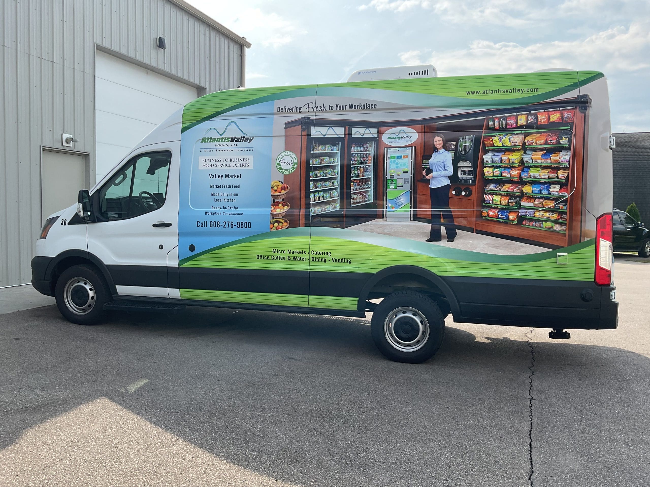 Atlantis Valley Market van, featuring custom fleet graphics, is parked next to a commercial building. The van advertises contact info and a woman using the market services