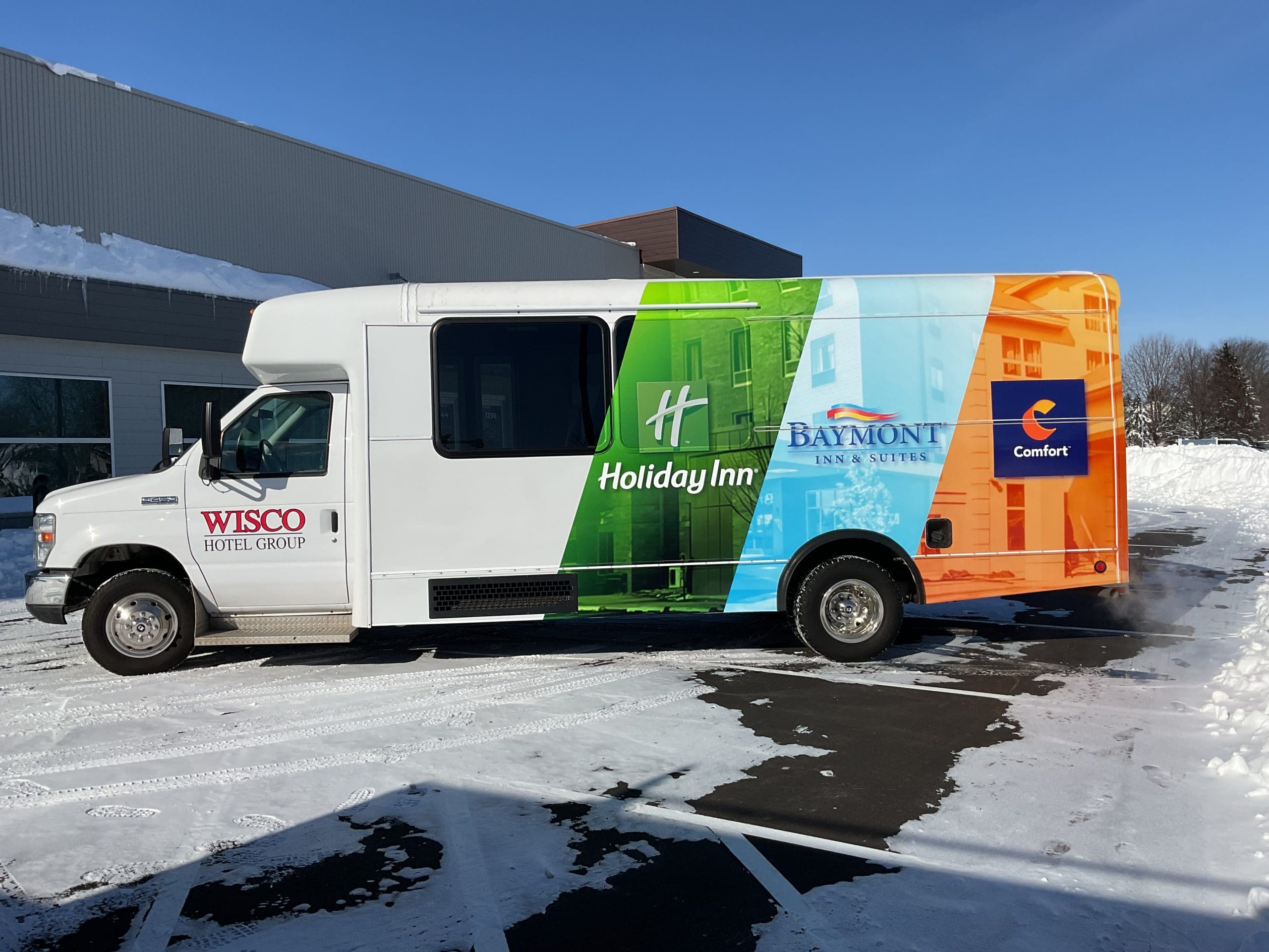 Hotel transportation bus, featuring custom fleet graphics, is parked in a snowy parking lot. Wisco Hotel group logo is on the driver door with the printed hotel partners near the back