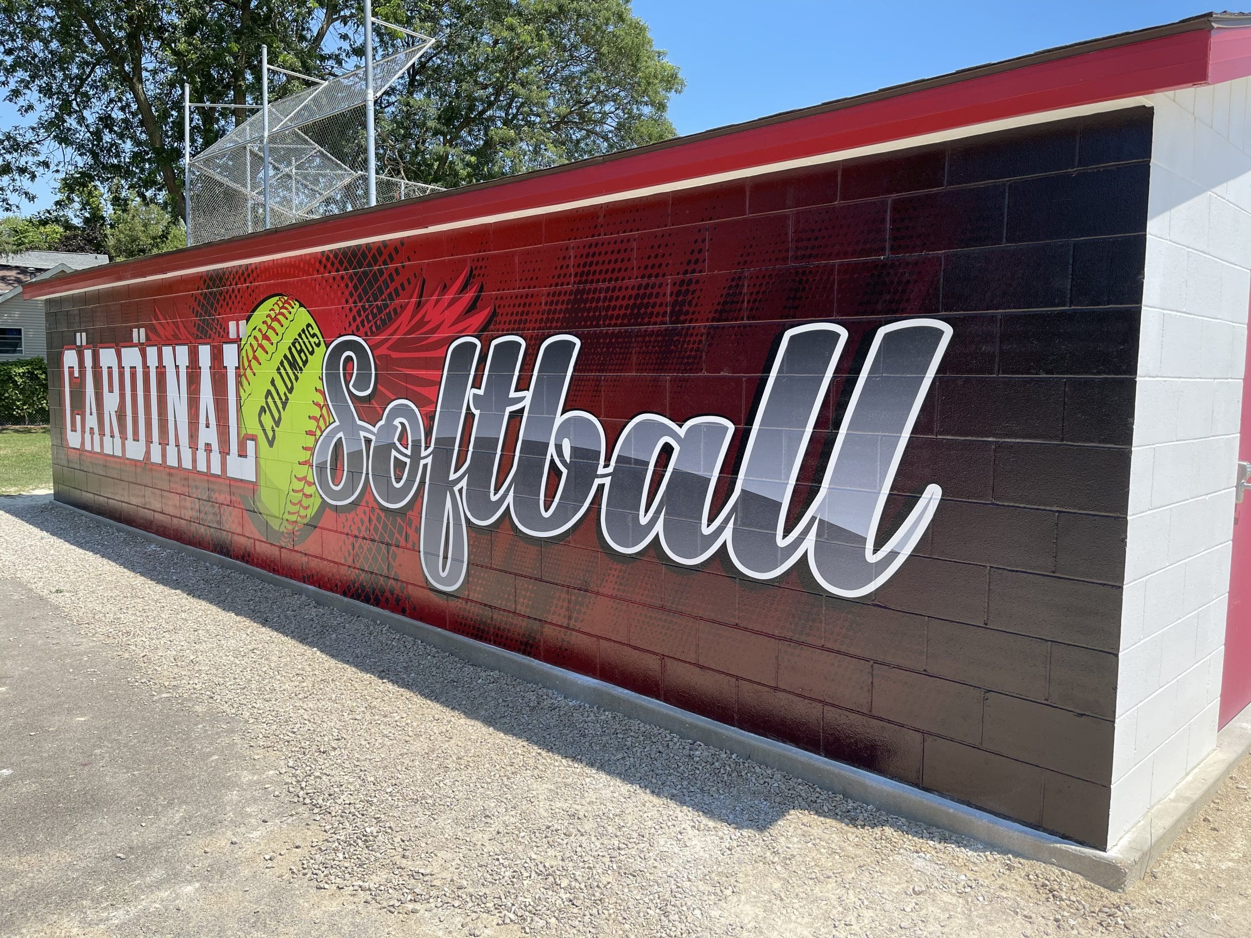 Softball Graphics banner on an outdoor wall behind a dugout