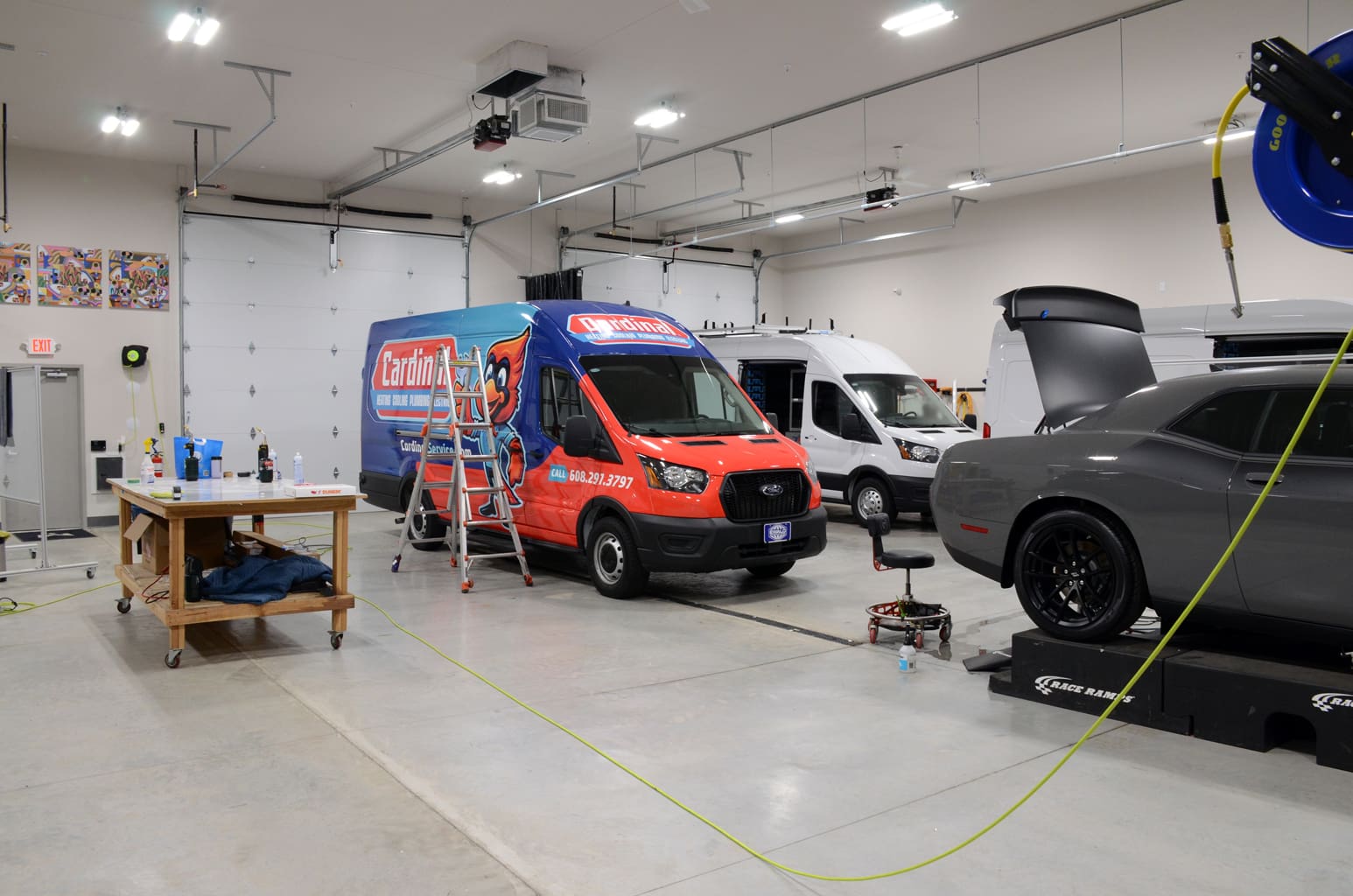 Design shop for fleet graphics with a plumbing company van and a white van being worked on. A dodge charger is also partially seen with the trunk open