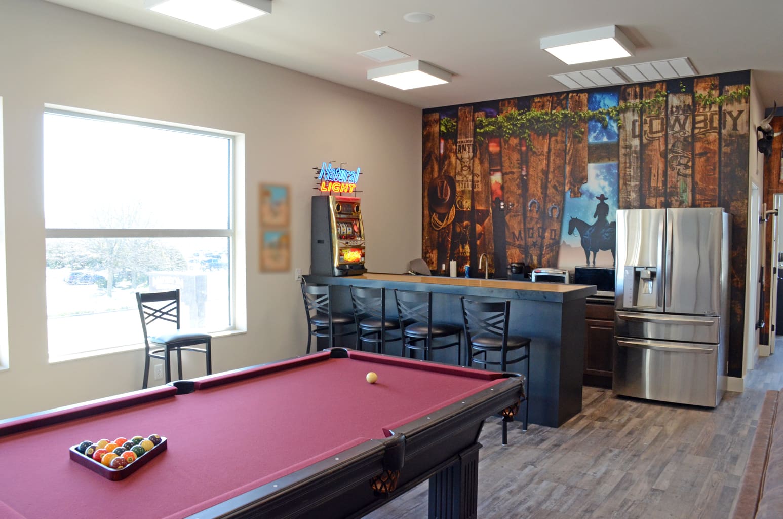 Club recreation room for Madison Graphics Company showing a pool table in the middle of a room with a drink bar and fridge. A cowboy wall mural is behind the bar